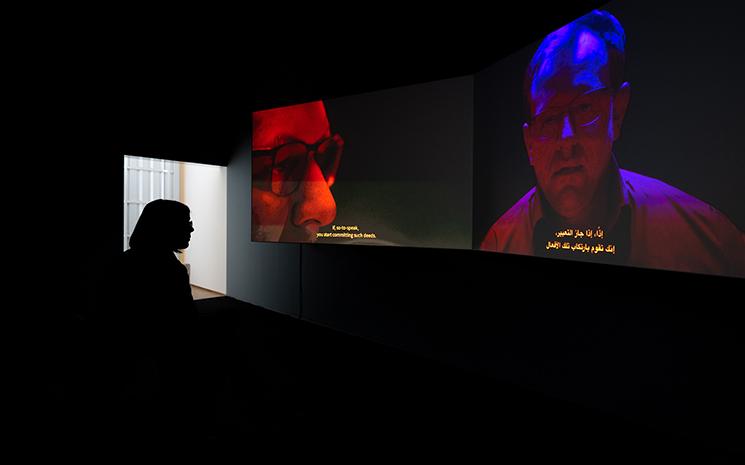 Une personne regarde un écran aux couleurs bleues et rouges diffusant le film de Mario Pfeifer