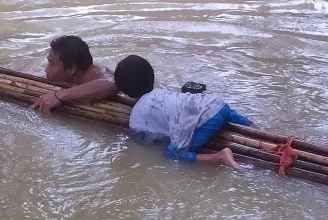 Un homme et son enfant dans l'eau, aggripes à un tronc d'arbre