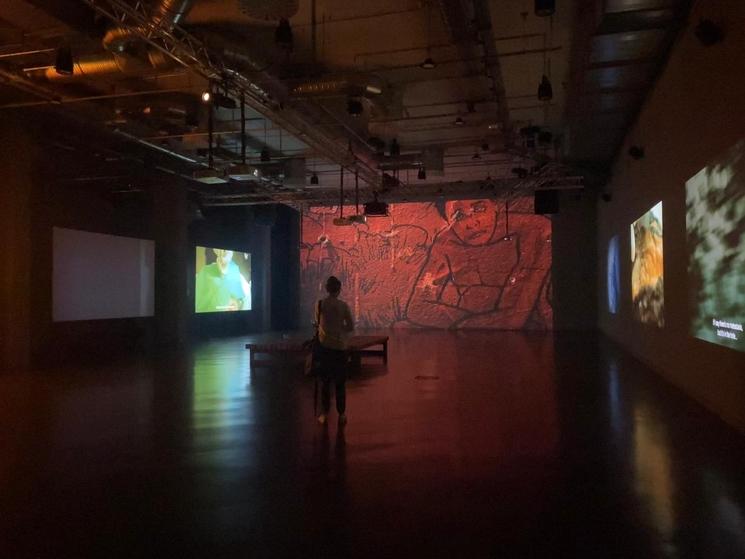 Salle avec de nombreux écrans et quelques visiteurs qui les regardent