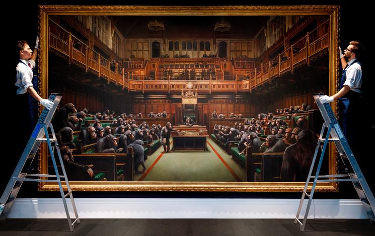 Oeuvre de Bansky en train d'être suspendue par deux hommes