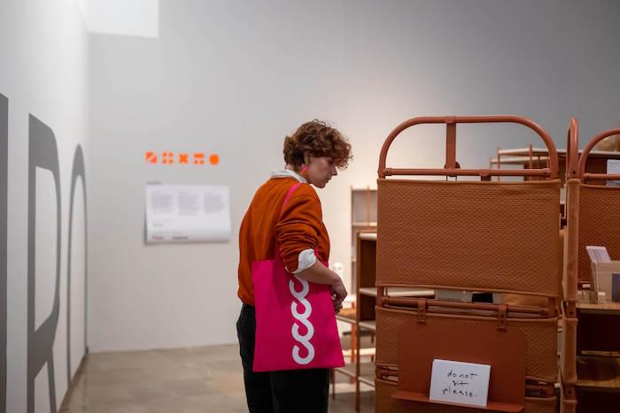 Une personne avec un sac violet du cccc en train de regarder des chaises lors d'une exposition