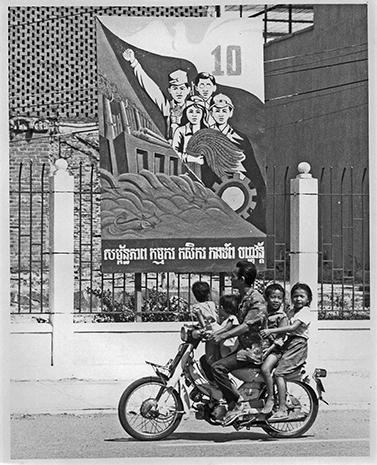 Family on a motorcyle passing poster celebrating 10 yeaer from the liberation of the khmer Rouge Phnom Penh, February 1989_@Alan Crumlish.