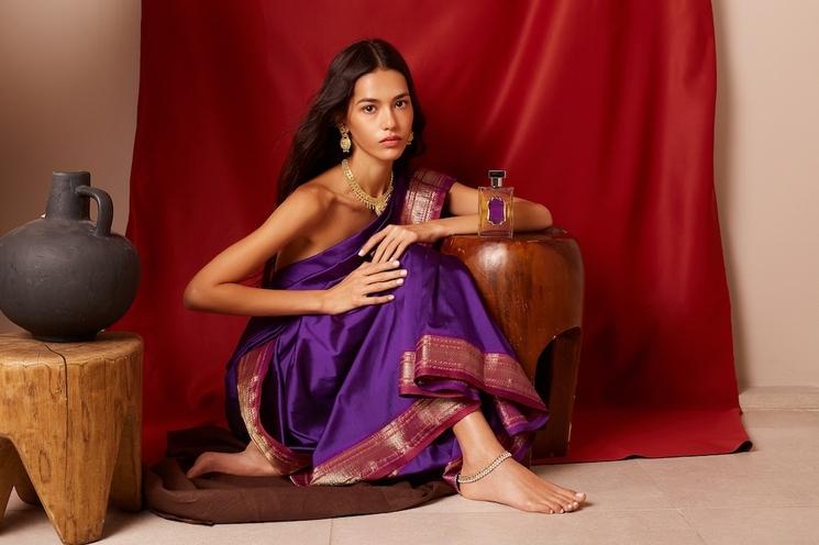 femme avec un sari violet accroupi posant à coté D'un parfum rideau rouge table basse bois vase gris