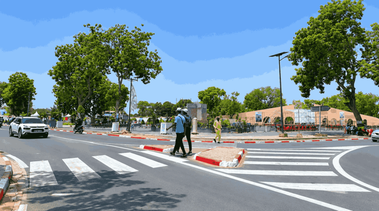 Carrefour arboré à Thiès avec passage piéton, circulation urbaine et espace public verdoyant sous un ciel ensoleillé.
