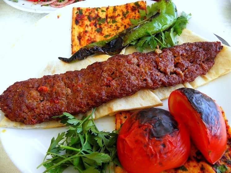 Adana kebabı traditionnel, kebab haché épicé grillé sur broche plate, servi avec tomates et poivrons