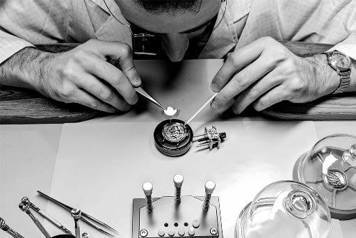 photo noir et blanc d'un horloger en train de reparer mecanismes de montres anciennes