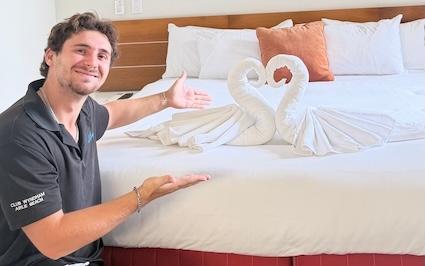 Un homme pose devant un lit avec une serviette en forme de cygne