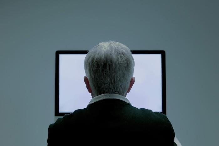 senior aux cheveux blancs de dos devant l'écran blanc de son ordinateur symbolisant l'absence de pistes professionnelles