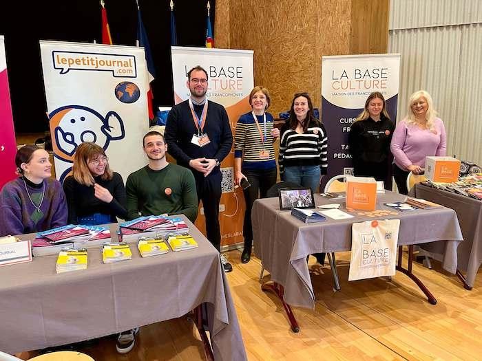 Des personnes posant devant les stands de La Base Culture et de lepetitjournal.com au Lycée français de Valence