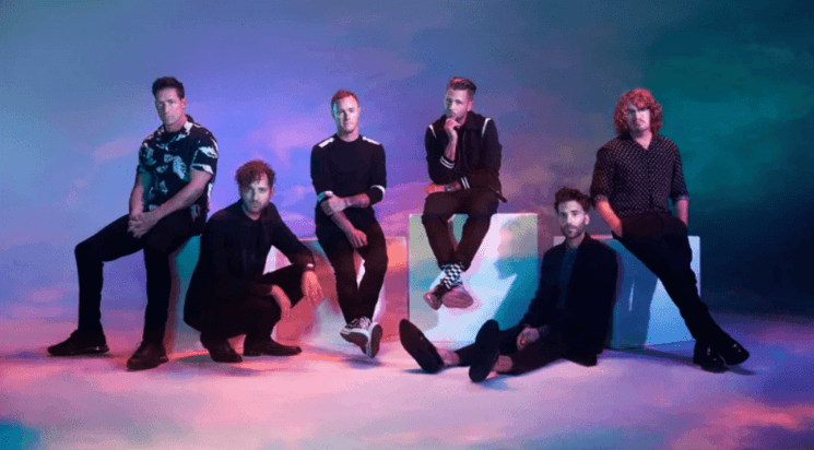 Photo promotionnelle du groupe OneRepublic avec Ryan Tedder et ses musiciens, dans une ambiance lumineuse et colorée.