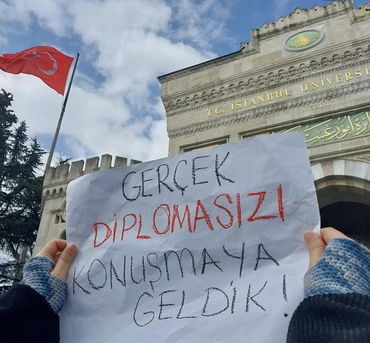 Étudiant manifestant devant l’Université d’Istanbul avec une pancarte sur la légitimité des diplômes
