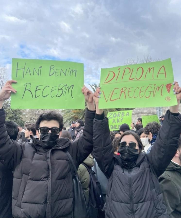 Deux jeunes manifestants tenant des pancartes vertes sur une promesse de diplôme non tenue