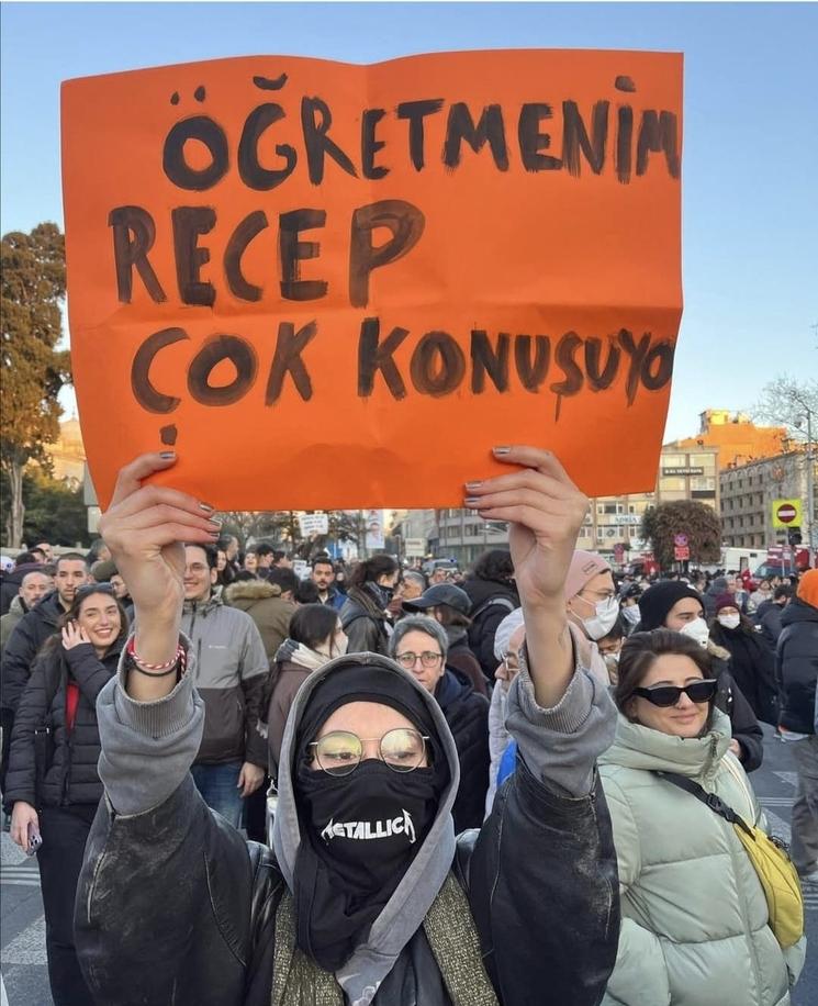 Étudiante brandissant une pancarte orange critiquant un dirigeant par dérision scolaire