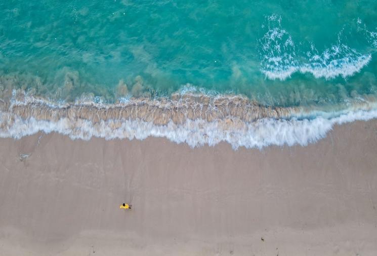 plage d'eau turquoise vue du ciel avec une personne sur la plage en t-shirt jaune