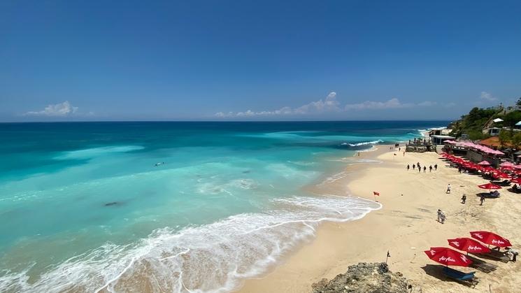 plage de sable blanc et d'eaux turquoises avec transat et parasols rouges et ciel bleu
