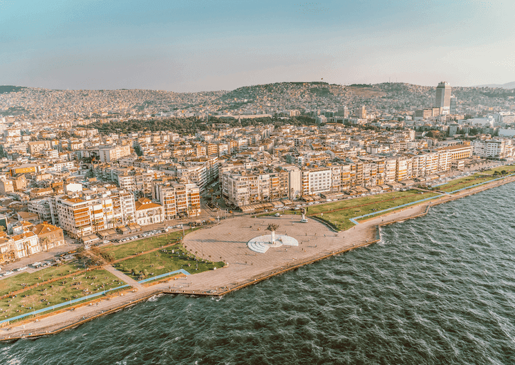 Vue aérienne de la promenade du Kordon à Izmir, Turquie, avec ses espaces verts en bord de mer, des bâtiments urbains et un coucher de soleil illuminant la baie d’Izmir.