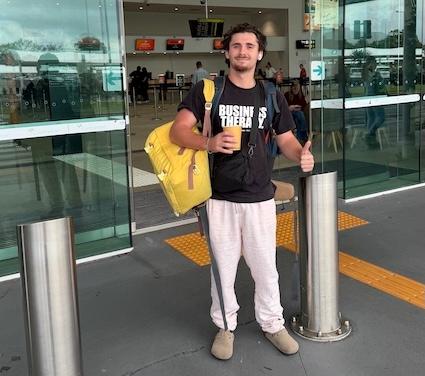 Un homme pose devant un aéroport avec ses sacs