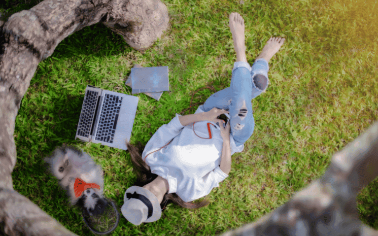 Une personne allongée sous un arbre, avec son ordinateur à côté, symbole qu'elle cherche un meilleur équilibre entre sa vie personnelle et sa vie professionnelle en 2023
