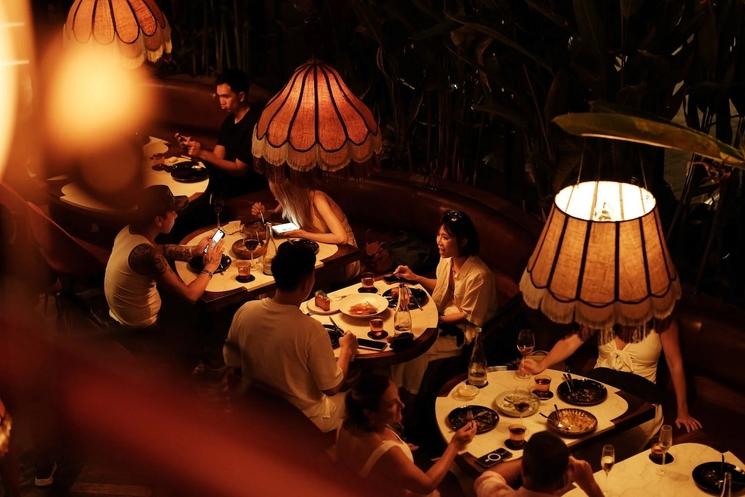 restaurant santenara à canggu, bali, avec descouples qui dînent sur des tables rondes dans une lumière tamisée