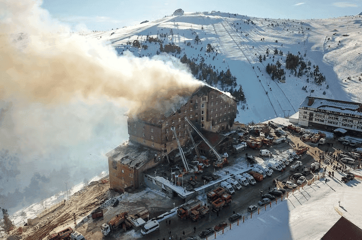 Vue aérienne du Grand Kartal Hotel en feu dans la station de ski de Kartalkaya, Turquie, entouré par des équipes de pompiers et des véhicules d'intervention, janvier 2025.