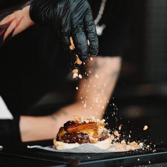 une personne en train de saler un hamburger à The Chapions Burger