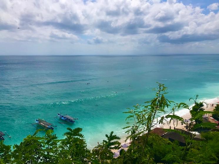 vue de loin sur la plage uluwatu thomas beach avec palmiers et végétation au premier plan et mer turquoi au second plan