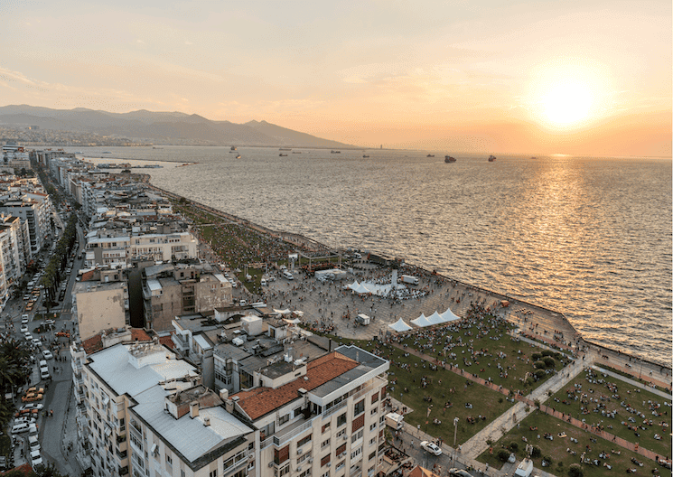 Vue aérienne du quartier d’Alsancak à Izmir, montrant la promenade en bord de mer au coucher du soleil, avec des bâtiments modernes, des espaces verts et une ambiance animée.