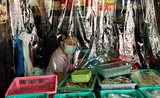 Une vendeuse thailandaise derriere un rideau plastifie anti-coronavirus