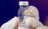 Fiolle de vaccin anti corrona tenue dans une main recouverte de gant en plastique
