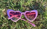 Des lunettes roses en forme de cœur posées dans le gazon