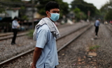 Un Thailandais portant un masque marche le long d'une voie ferree