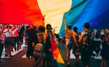 plusieurs personnes défilent sous un drapeau arc-en-ciel LGBTI+