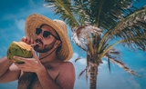 un homme déguste une noix de coco sous les palmiers