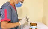 Un docteur avec un masque hygiènique, tenant une seringue, avec une peluche