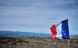 Un drapeau français flotte en haute d'une montagne sous un ciel bleu 