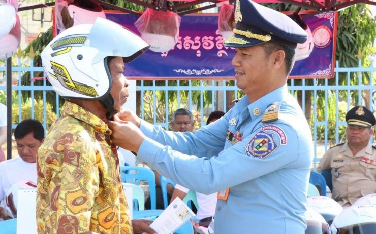 un policier cambodgien donnant un casque à un motocycliste pour éviter un accident