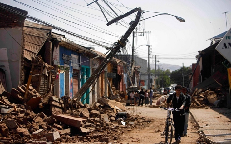 Un homme tient son vélo à la main à côté de bâtiments détruits par le tremblement de terre