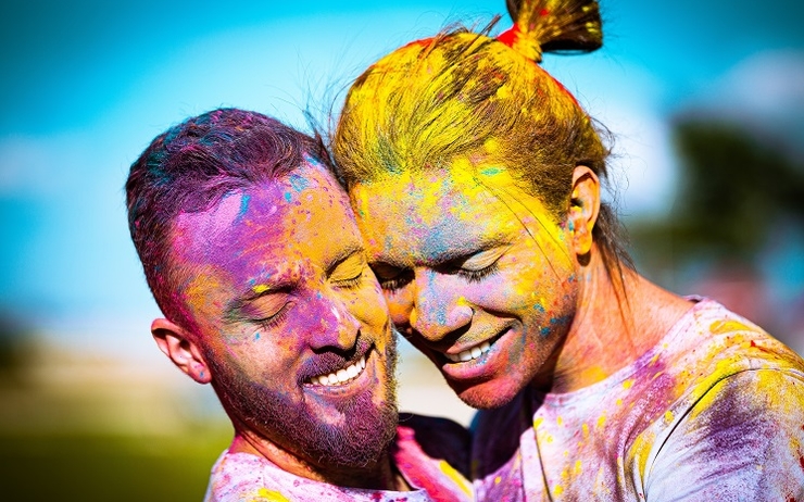 Deux hommes souriant dans les bras l'un de l'autre, recouverts de peinture multicolore