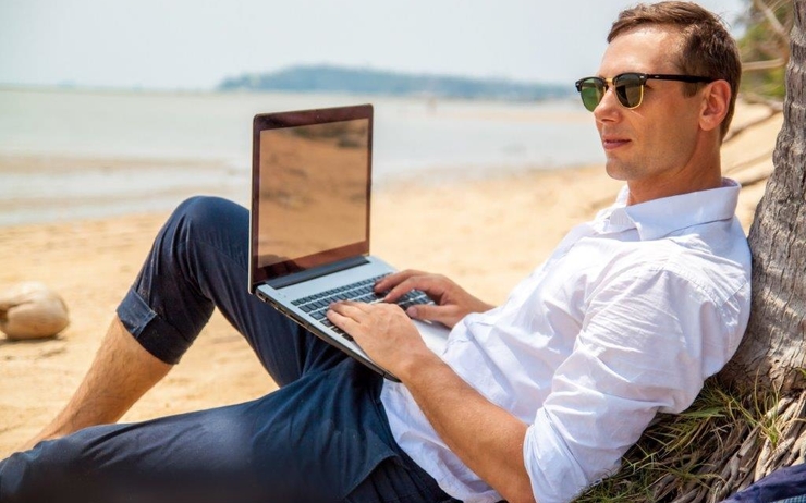 homme qui investit en SCPI depuis son ordinateur sur la plage 