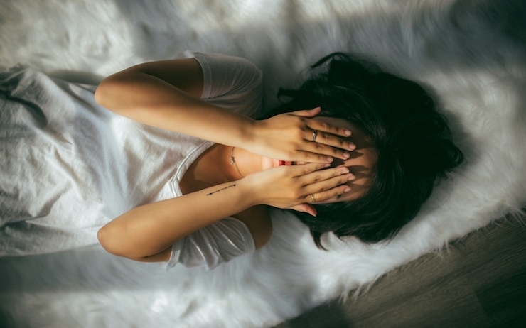 Une femme couchée dans son lit qui se tient la tête entre les deux mains 