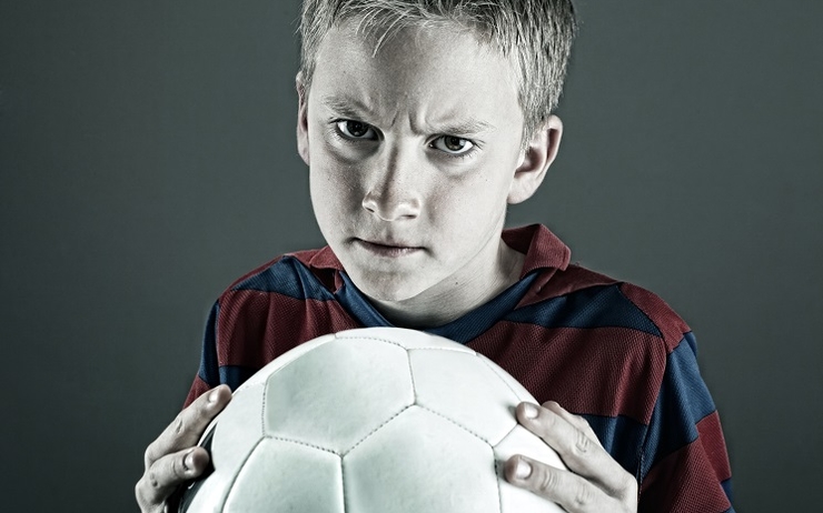 Un enfant tenant un balon de foot, l'air très contrarié