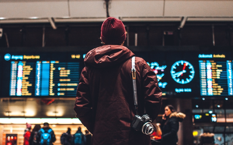 Un homme se tient devant les panneaux d'arrivées à l'aéroport 
