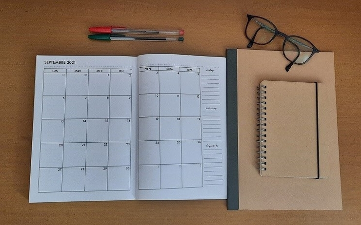 un calendrier ouvert avec carnet, un stylo et des lunettes sur un bureau