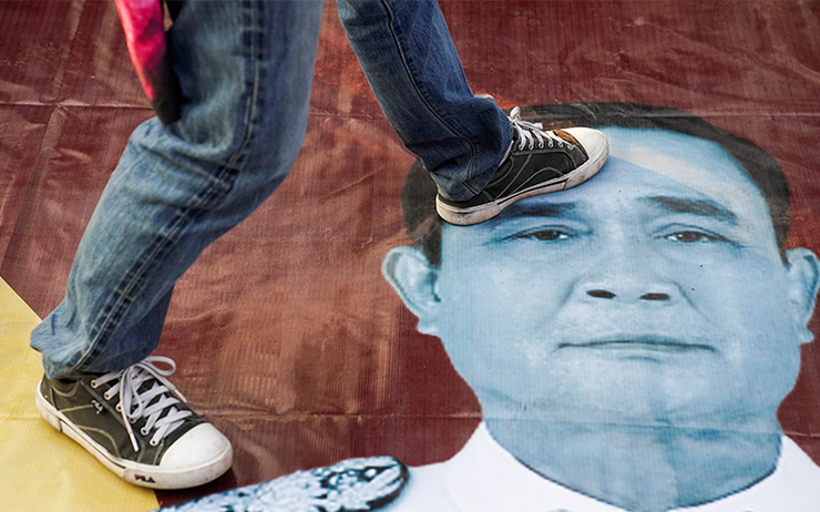 Un manifestant thailandais pose le pied sur la photo du Premier ministre Prayuth Chan-O-Cha