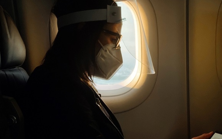 une personne avec masque regarde son telephone dans un avion