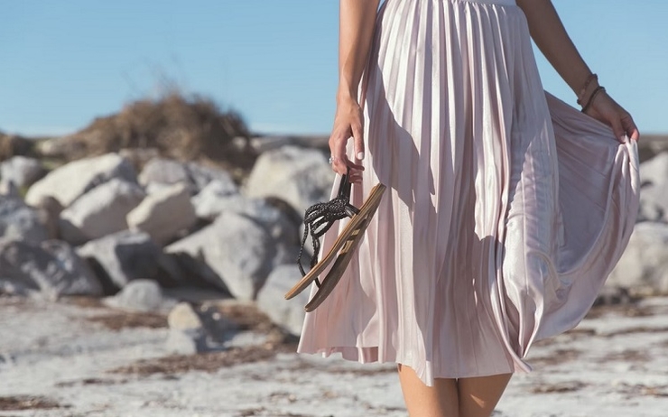 une femme porte une jupe et des sandales sur le sable