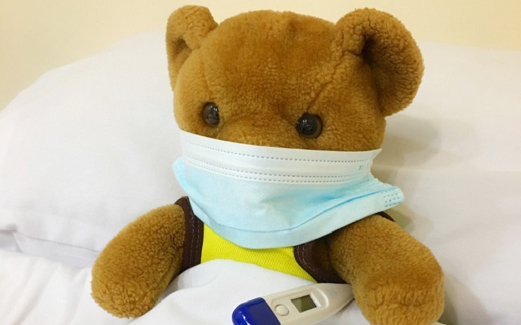 Un ours en peluche dans un lit avec un masque et un thermomètre