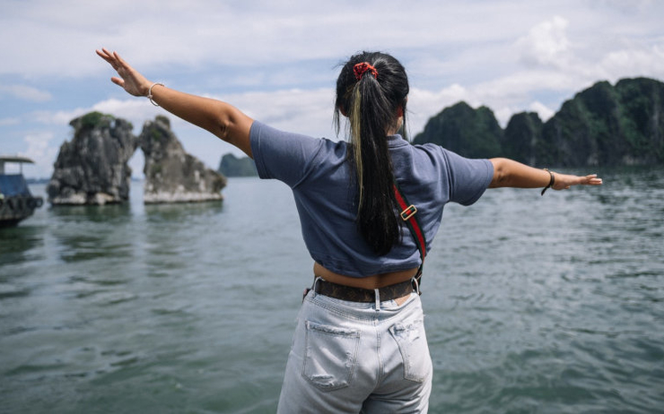 Une femme de dos écartant les bras face à la Baie d'Ha Long