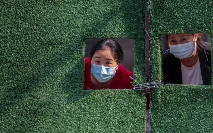deux chinois regardent par une barriere avec des masques