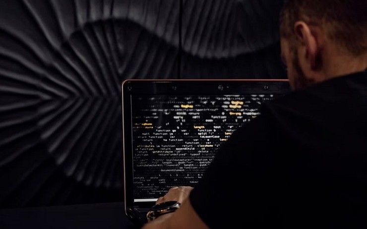 un homme en noir rentre un code sur son ordinateur